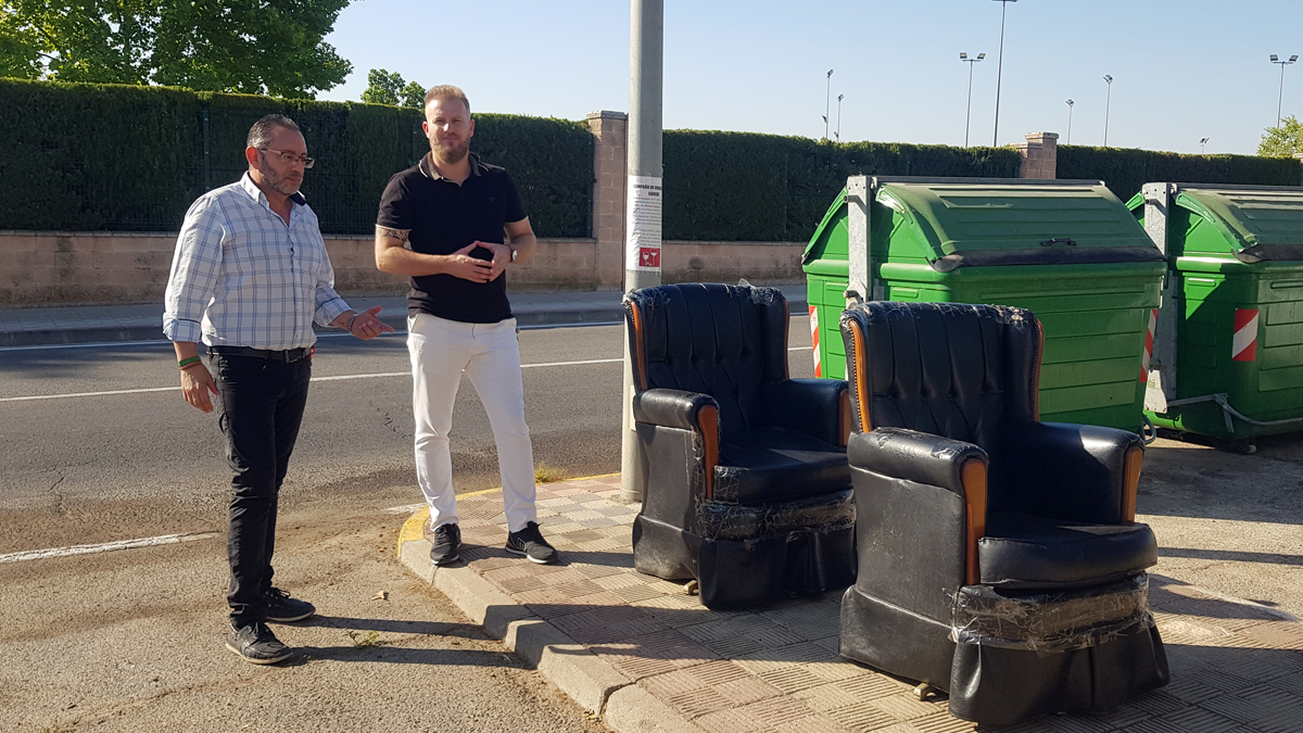 Miembros de VOX junto a varios muebles depositados junto a contenedores en Dos Hermanas